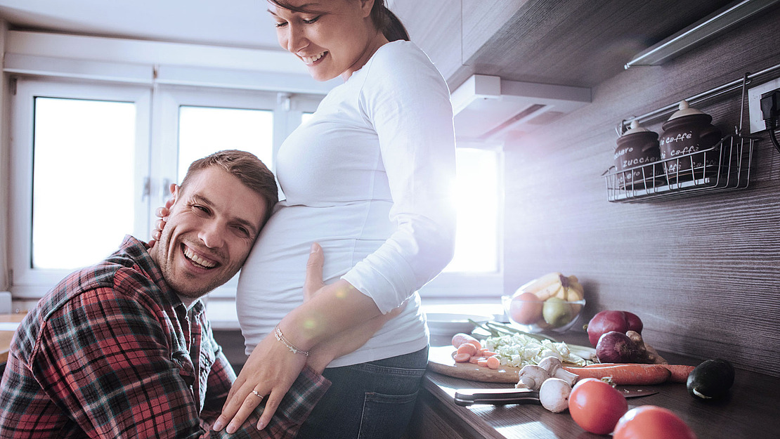 Mann legt sein Ohr auf den Bauch seiner schwangeren Frau