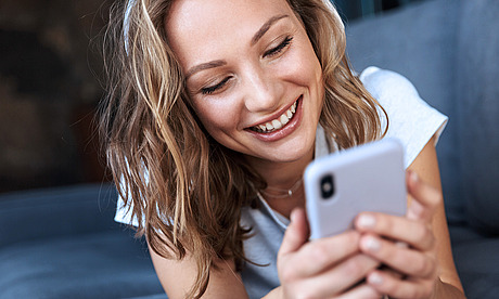Frau benutzt liegend Smartphone auf dem Sofa.