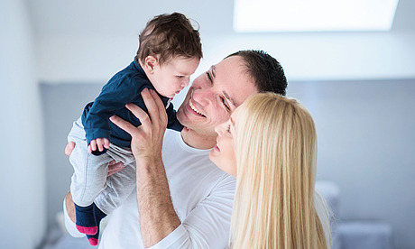 Eine junges Paar hebt deren gemeinsames Baby in die Luft