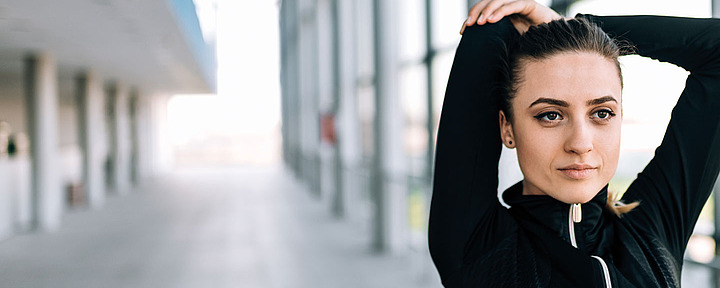 Junge Frau macht Dehnübung. Sie hält ihre Arme über dem Kopf.