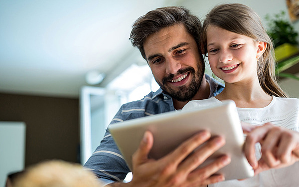 Vater mit Tochter schaut auf Tablet.