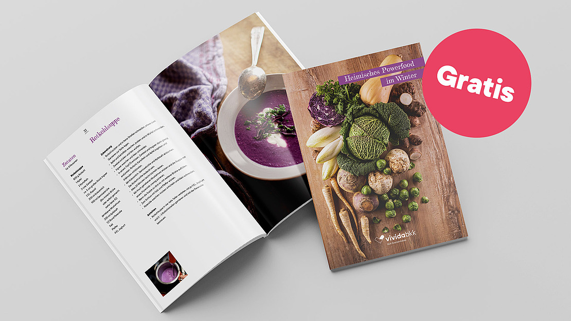 Zwei offene und geschlossene Kochbücher mit einem Wintergemüse-Thema werden auf einer grauen Fläche ausgestellt. Das geschlossene Buch zeigt verschiedene Gemüsesorten, während die aufgeschlagenen Seiten ein lila Suppenrezept zeigen. Auf einem rosa Kreis steht "Gratis".