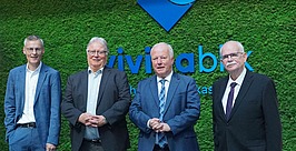 Vier Männer in Anzügen stehen vor einer grünen Wand und posieren für ein Gruppenfoto.