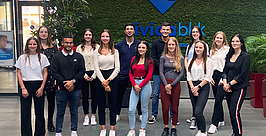 Eine Gruppe von dreizehn jungen Erwachsenen steht lächelnd vor einer grünen Wand mit dem „civitasblik“-Logo. Die Gruppe ist leger gekleidet und scheint für ein Gruppenfoto zu posieren.