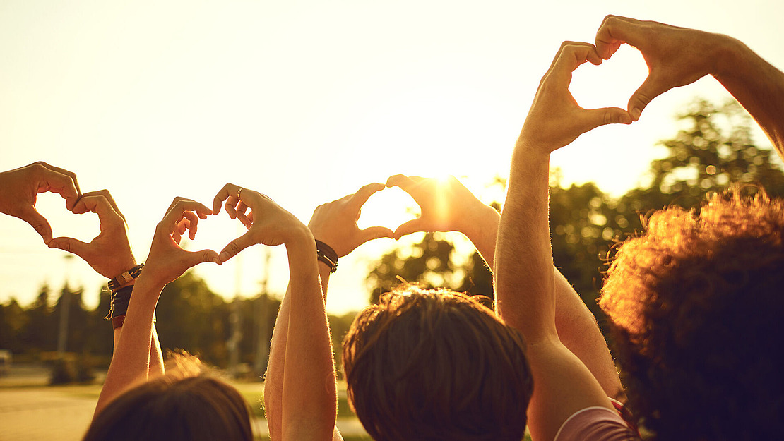 Vier Menschen zeigen mit Ihren Händen ein Herzsymbol Richtung Himmel.