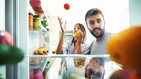 Eine Frau und ein Mann stehen vor einem geöffneten Kühlschrank und schauen rein