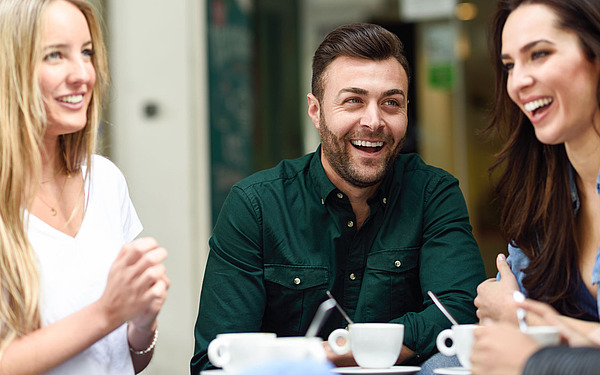Zwei junge Frauen und ein Mann sitzen in einem Café