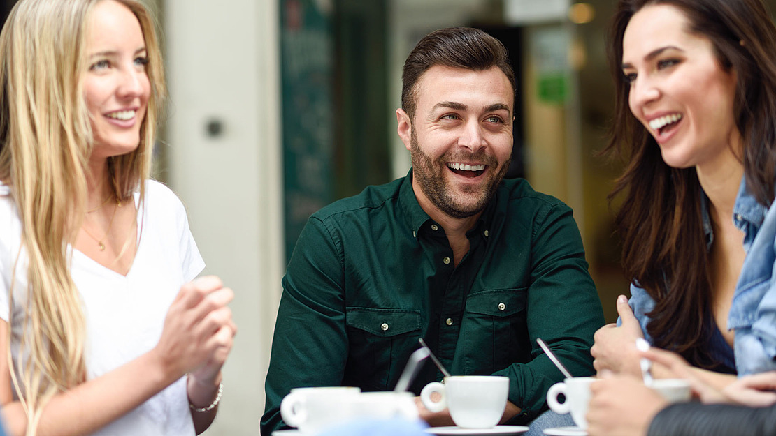 Zwei junge Frauen und ein Mann sitzen in einem Café