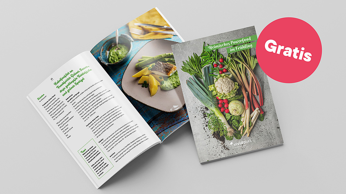 Ein Kochbuch mit dem Titel "Heimisches Powerfood im Frühling" mit einem Einband, der frisches Gemüse zeigt. Daneben befindet sich eine aufgeschlagene Seite mit Rezepten und Fotos von Lebensmitteln. In der oberen rechten Ecke ist ein rosa Kreis mit "Gratis" abgebildet.