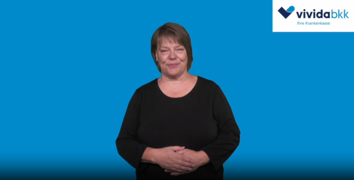 Eine Frau, die ein schwarzes Oberteil trägt, steht vor einem einfarbig blauen Hintergrund.